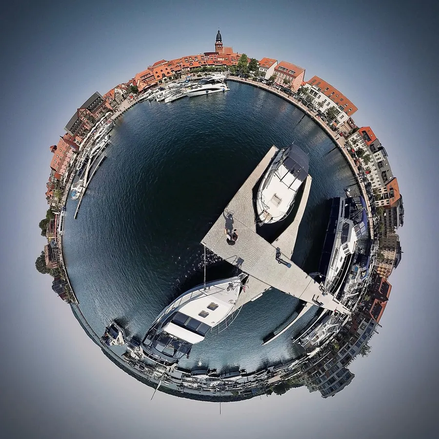 Tiny Planet vom Stadthafen in Waren (Müritz): ein Steg mit Booten in der Mitte, rundherum die Häuser der Altstadt und der Kirchturm