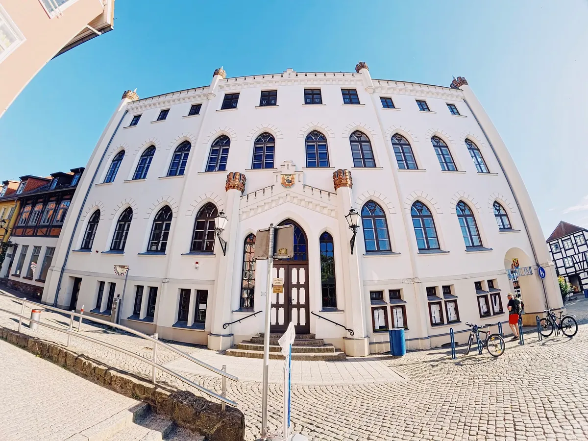 Weißes neugotisches Rathaus mit Spitzbogenfenstern am Neuen Markt in Waren (Müritz), Weitwinkelaufnahme unter blauem Himmel